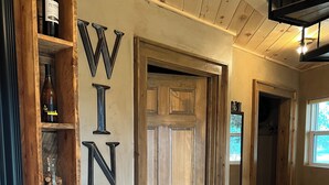 Una botellera de madera con botellas y tapones, una puerta de madera con un letrero que dice 'WINE', y un piso de baldosas.