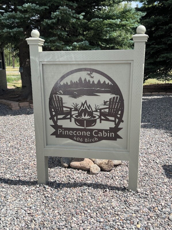 A sign for Pinecone Cabin at 406 Birch, featuring a campfire and chairs around it. - The Pinecone Cabin. Twenty minutes from Wolf Creek Pass. (South Fork)