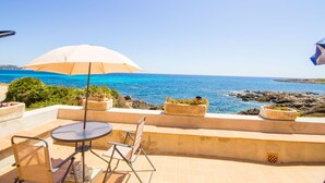 Une terrasse avec une table et des chaises, un parasol et une vue sur la mer.