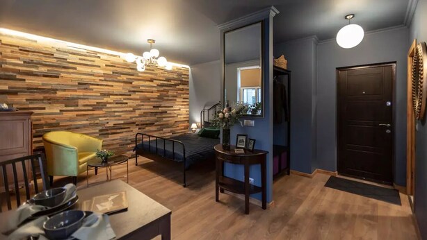 Un salon moderne avec un mur en bois, un fauteuil jaune, un lit, un miroir et une porte noire.