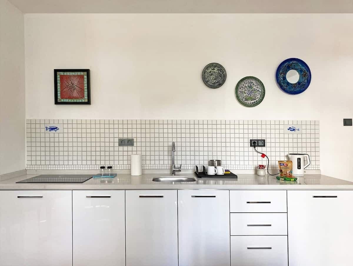 Una cocina moderna con armarios blancos, un lavamanos de acero inoxidable y un protector contra salpicaduras de azulejos.