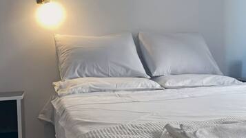 Un lit bien fait, avec du linge de lit blanc et des oreillers, une table de chevet avec une lampe et une petite armoire blanche.