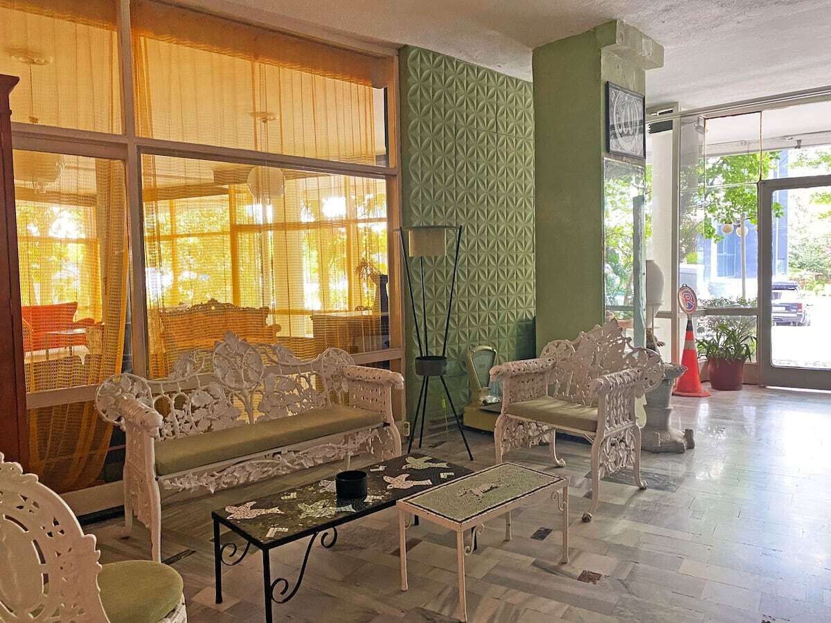 Un vestíbulo amplio con un gran ventanal, muebles blancos ornamentados y una pared texturizada de color verde.
