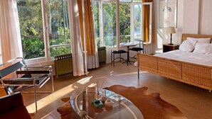 A modern bedroom with a large bed, a glass coffee table, a wicker chair, and a view of greenery through large windows. - Petek Pansiyon (Istanbul)