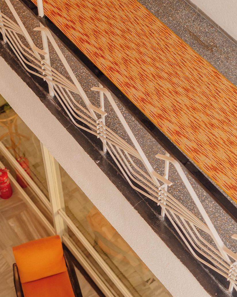 A close-up of a ceiling with a patterned orange and brown design, white beams, and a glass window below.