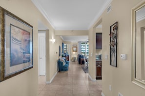 A hallway with a large framed picture, a blue armchair, a dining area, and a kitchen. - Bay Views~Walk2Beach-Lazy 🌴River-3BR Osprey 505 (Fort Walton Beach)