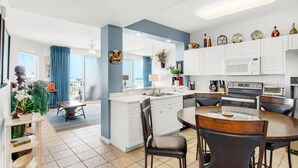 A modern kitchen with white cabinets, a central island, and a dining area with a round table and chairs. - 🌊 Gulf Front~Pools~Walk 2 Beach~Beach SVC~2BR Destin West Gulfside 608 (Fort Walton Beach)
