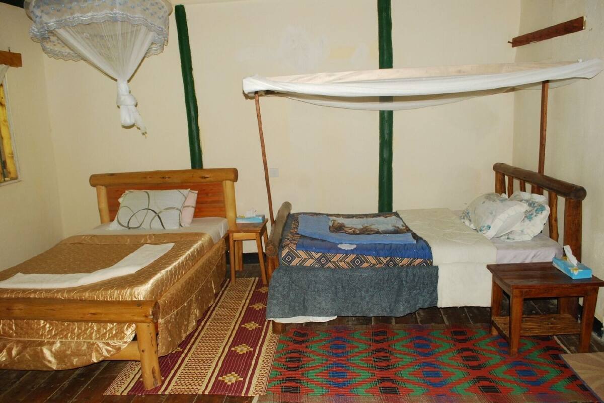 A room with two wooden beds, one with a canopy, and a patterned rug.
