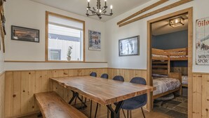 Un tavolo da pranzo in legno con panche, un lampadario, quadri incorniciati e un angolo con letto a castello.