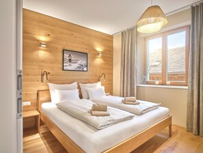 Un lit double avec du linge de lit blanc, une tête de lit en bois, une photo encadrée accrochée au mur et une fenêtre avec des rideaux.