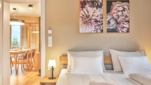 Ein Hotelzimmer mit Holzboden, einem Bett mit weißen Leinen, einem Nachttisch mit Lampe und zwei floralen Bildern an der Wand.