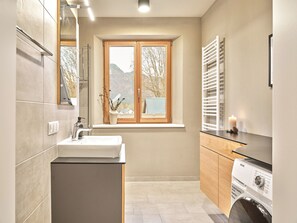 Une salle de bain moderne équipée d’un lavabo, d’un miroir, d’une fenêtre et d’un lave-linge.