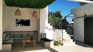 Un espacio exterior moderno con un sofá, una mesa de centro y dos lámparas colgantes.