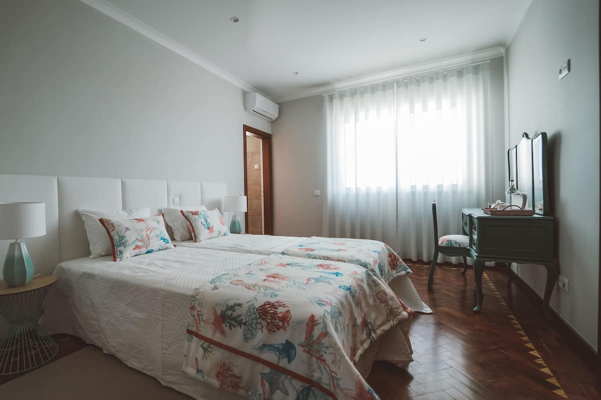 Ein Schlafzimmer mit zwei Betten, einem Schreibtisch, einem Stuhl und einem Fenster mit Vorhängen.