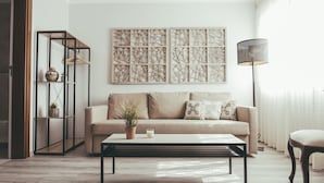 Una sala de estar con un sofá, una mesa de centro, una lámpara de pie y una obra de arte en la pared.