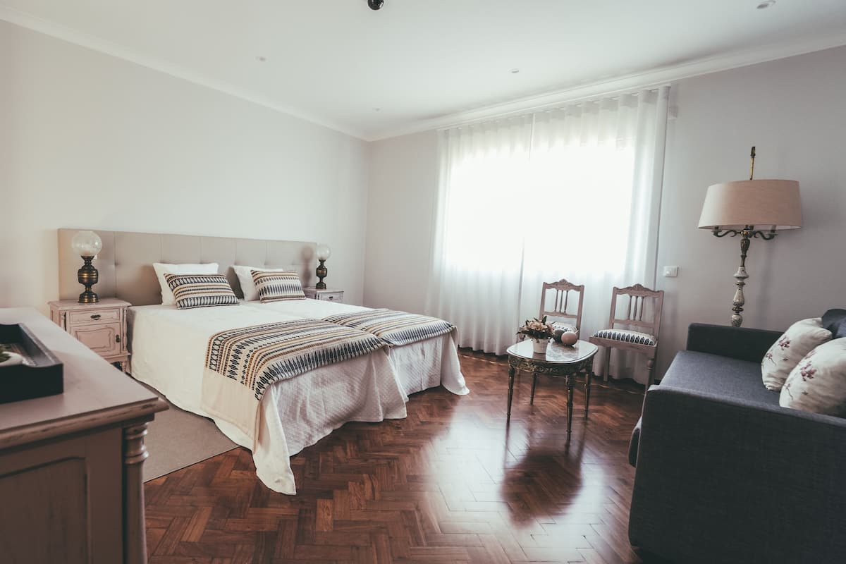 Ein ordentlich eingerichtetes Schlafzimmer mit einem großen Bett, Nachttischen, einem kleinen Tisch mit Blumen und einem Sessel.