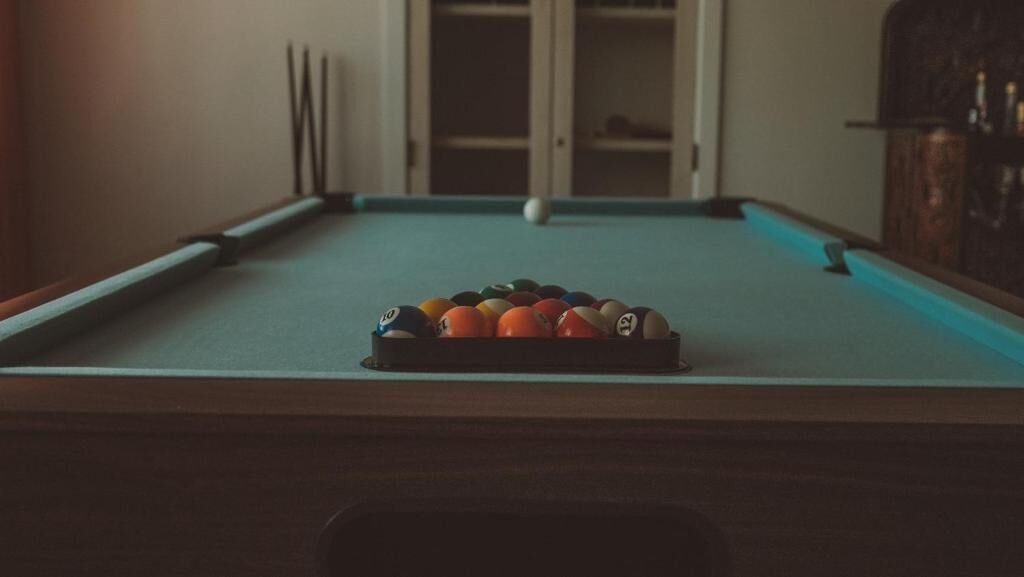 A pool table with balls arranged in a triangle formation, a cue stick, and a white ball in the center.