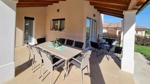 A covered patio with a table and chairs, a small window, and a view of a house in the background. - New modern villa with private pool 7 km from the sea. (Rovinjsko Selo)
