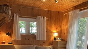 Une chambre dans une cabane en bois, avec un lit, des tables de chevet et une fenêtre avec des rideaux.