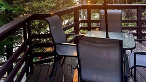 Une terrasse extérieure avec une table et des chaises, protégée par un grand parasol, entourée d’arbres et offrant une vue sur le coucher du soleil.