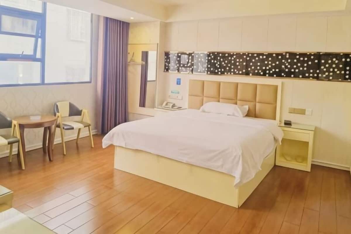 Una habitación de hotel con cama, mesita de noche, silla, escritorio y ventana con cortinas.