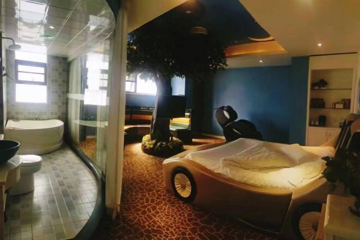 Una habitación con cama, una mesita, una silla, una escultura de árbol y una bañera.