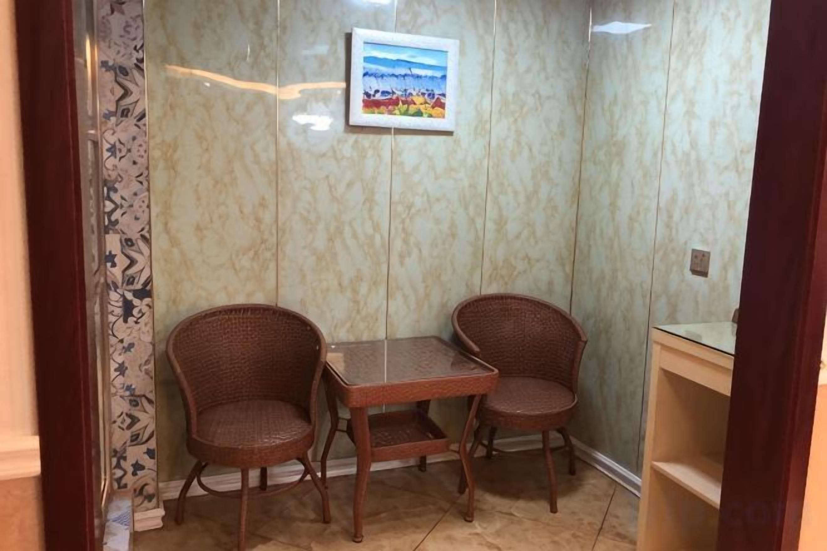 A corner room with two wicker chairs, a small table, and a framed picture on the wall.