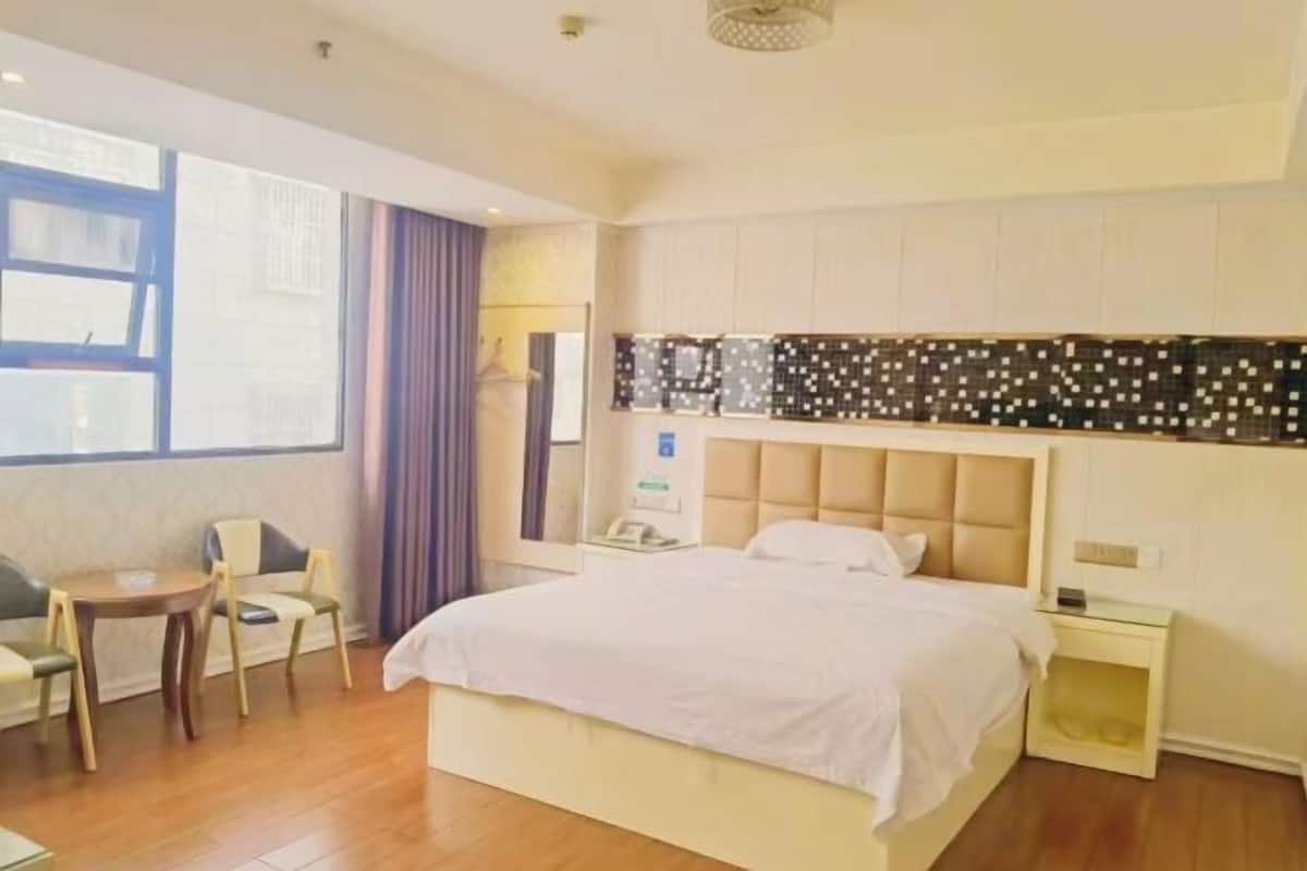 Habitación de hotel con una cama grande, una mesita con sillas, una mesita de noche y un ventanal con cortinas.