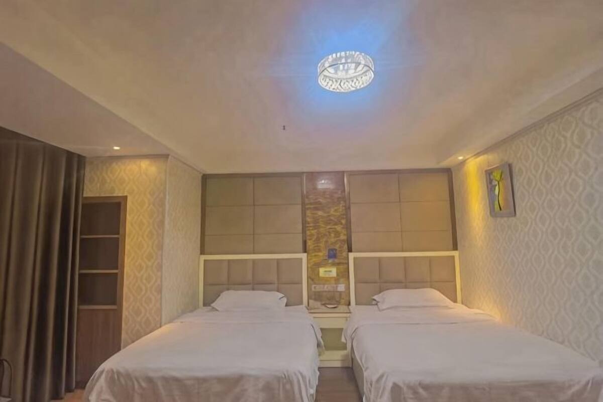 Habitación de hotel con dos camas, una araña, un armario y un papel tapiz estampado.