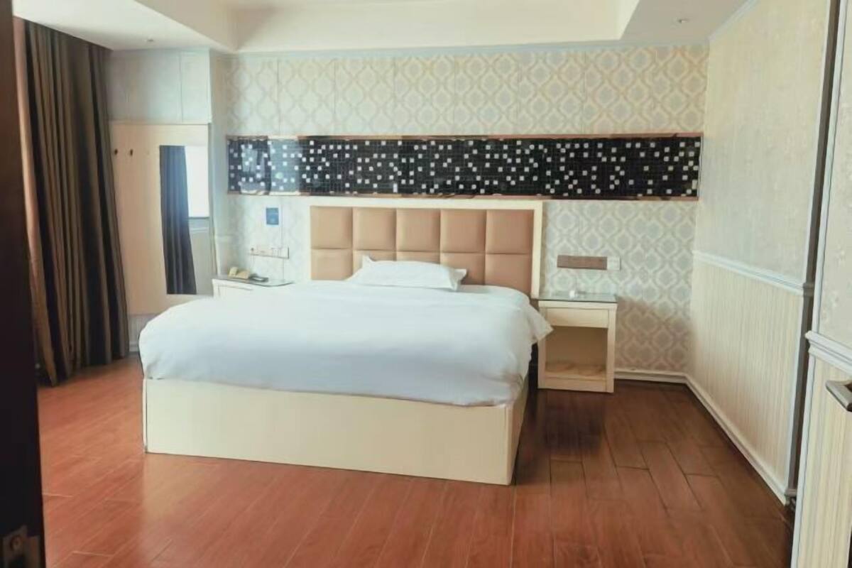 Habitación de hotel con cama, mesitas de noche, mesilla auxiliar, pared con diseño y ventana con cortinas.