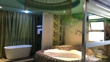 A room with a large bed, a bathtub, and a wall with a tree mural.