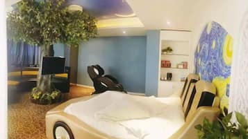 Hotellihuone, jossa on sänky, hierontatuoli, puu, taulu ja televisio.