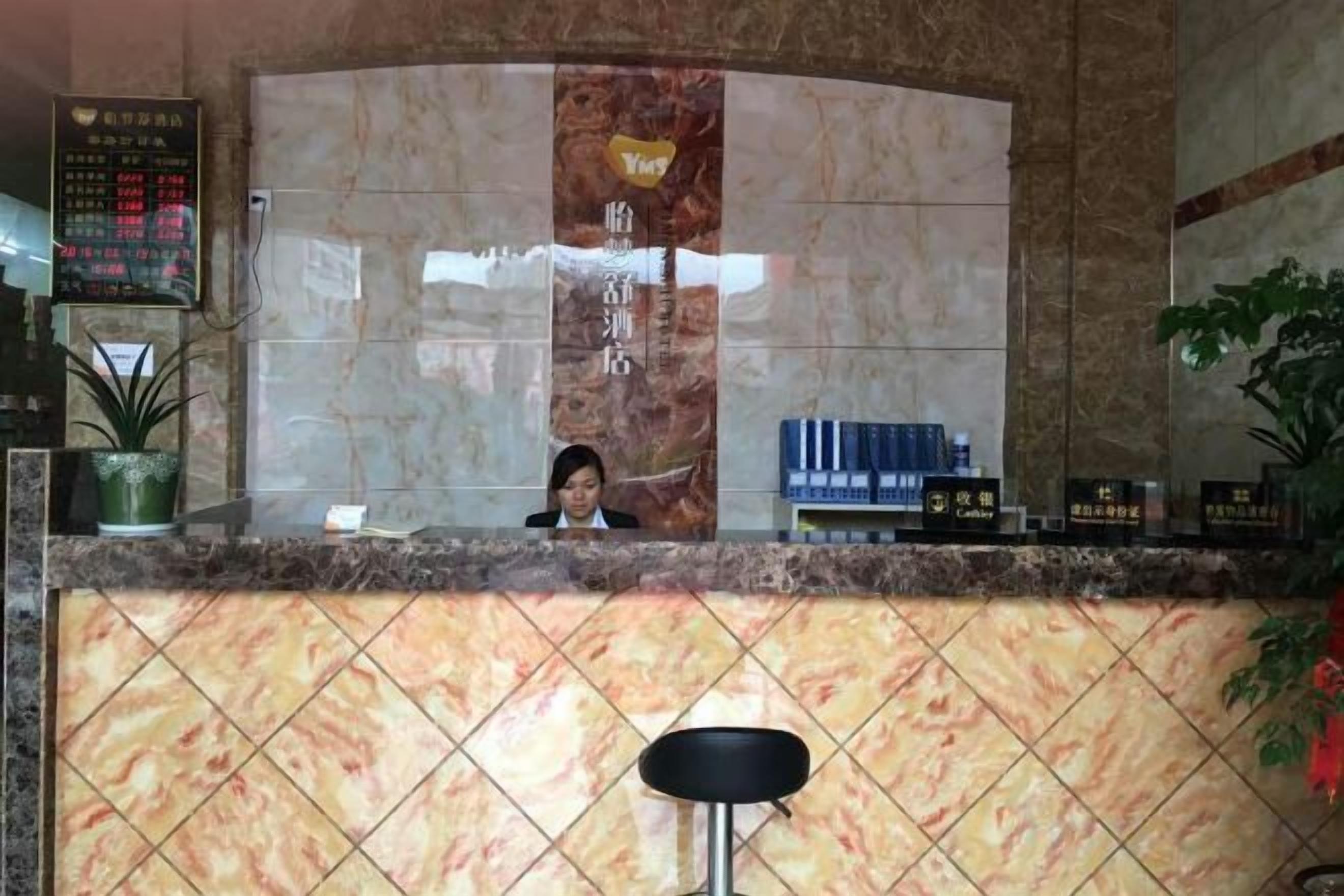 Un área de recepción con mostrador de mármol, una recepcionista sentada y una planta en maceta.