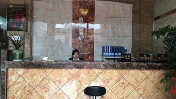 Un área de recepción con mostrador de mármol, una recepcionista sentada y una planta en maceta.
