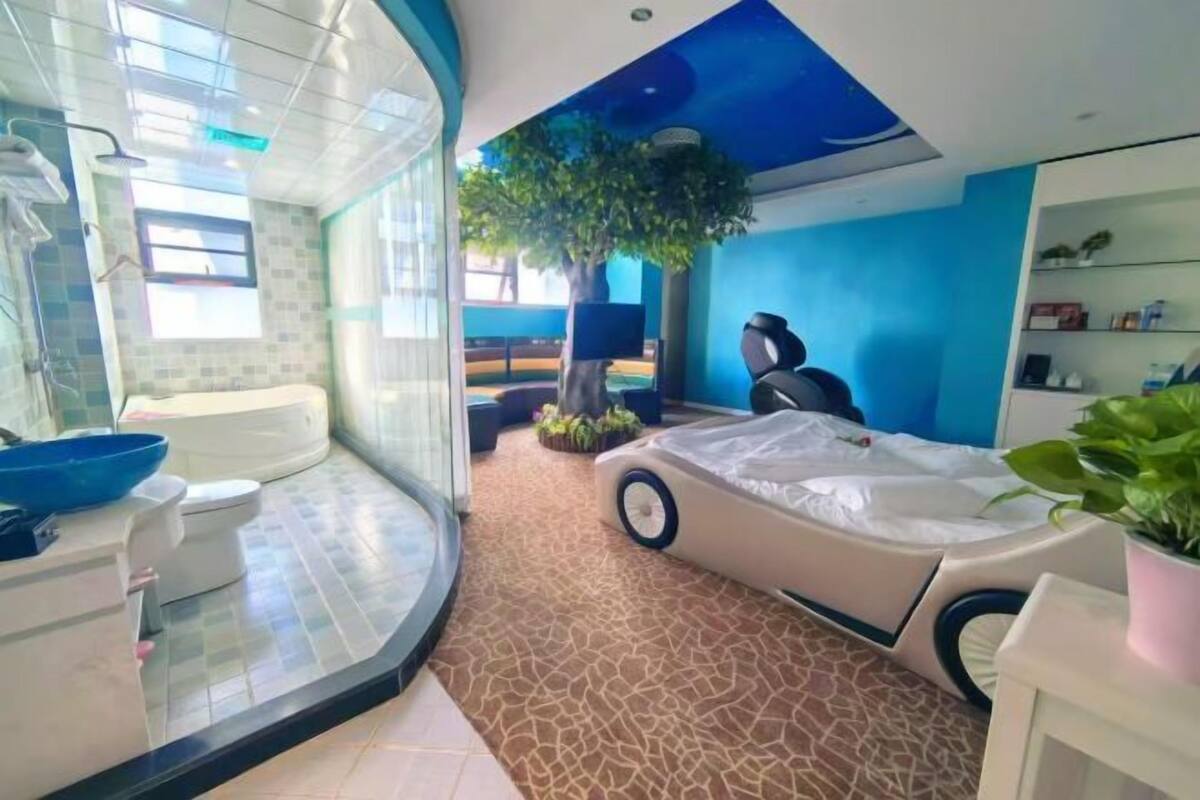 Un baño moderno con ducha de vidrio curvo, bañera y una cama con forma de coche original.