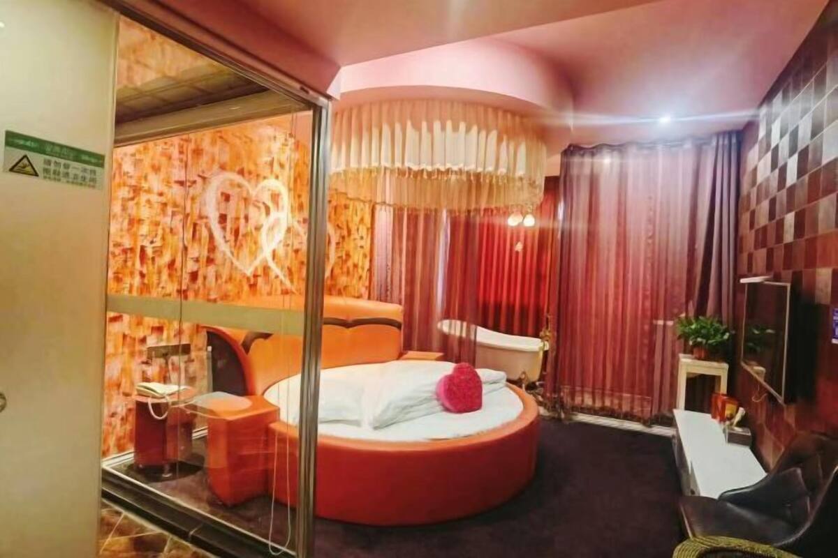 Una cama redonda con una lámpara en forma de corazón, una mesa circular y un televisor en la pared.