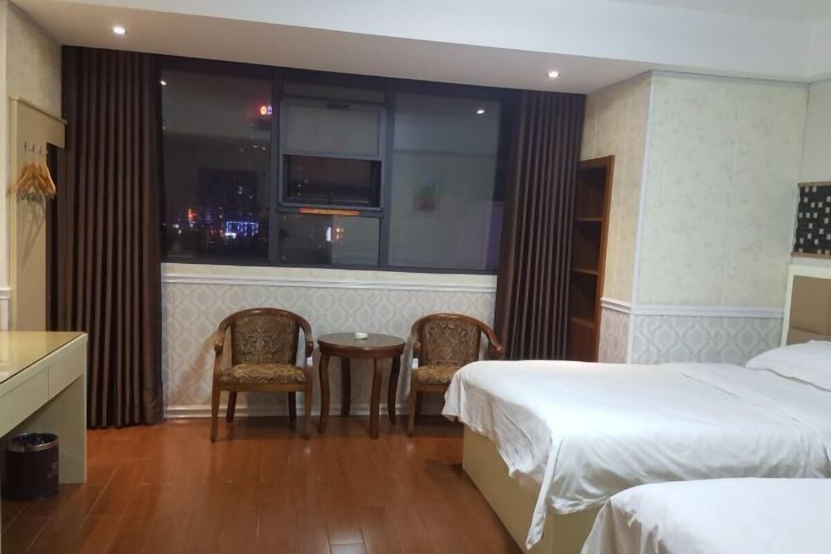 A hotel room with two beds, a small table, two chairs, a window with a view of the city at night, and a wardrobe.