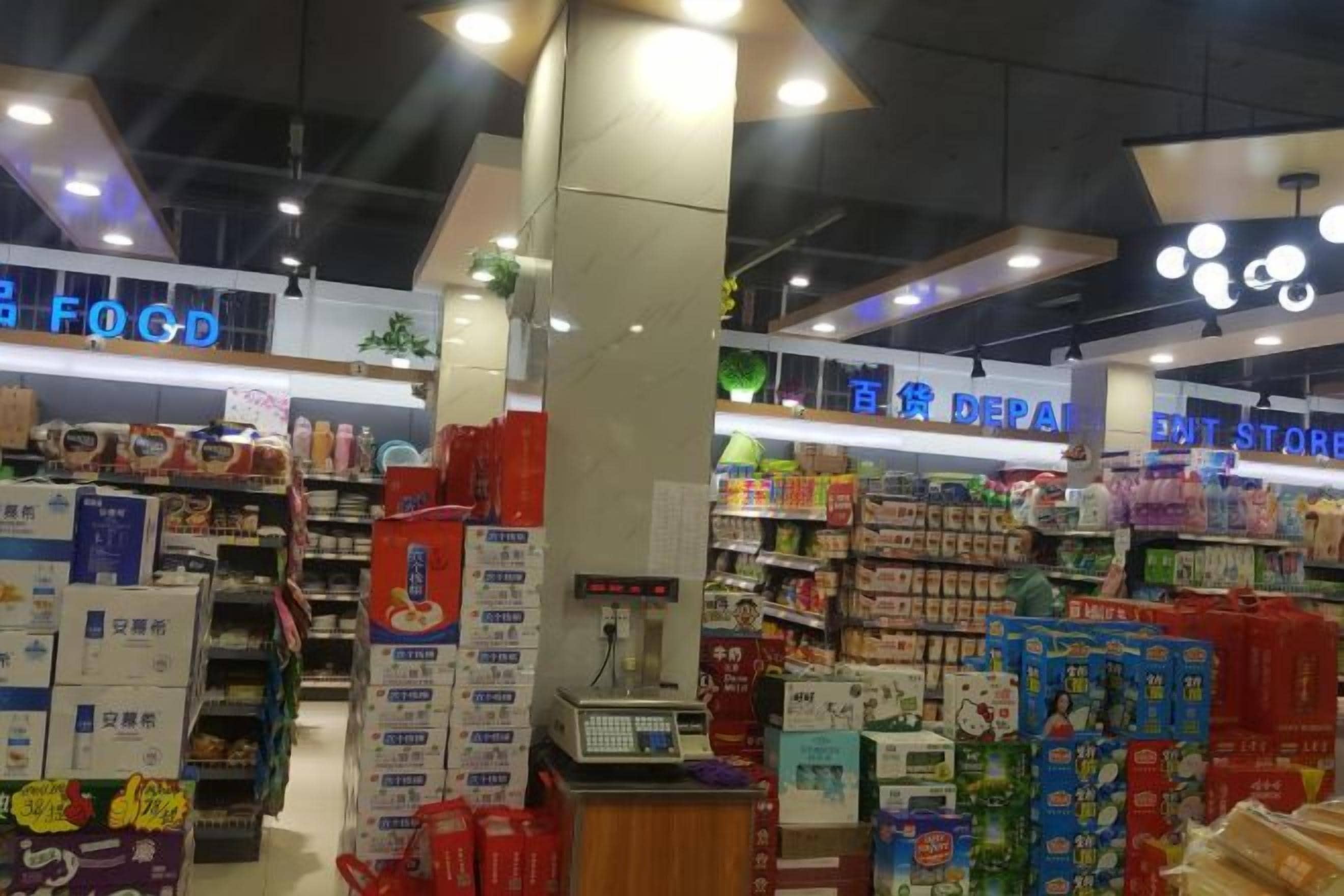 A supermarket interior with aisles stocked with various products, including boxed goods and household items.