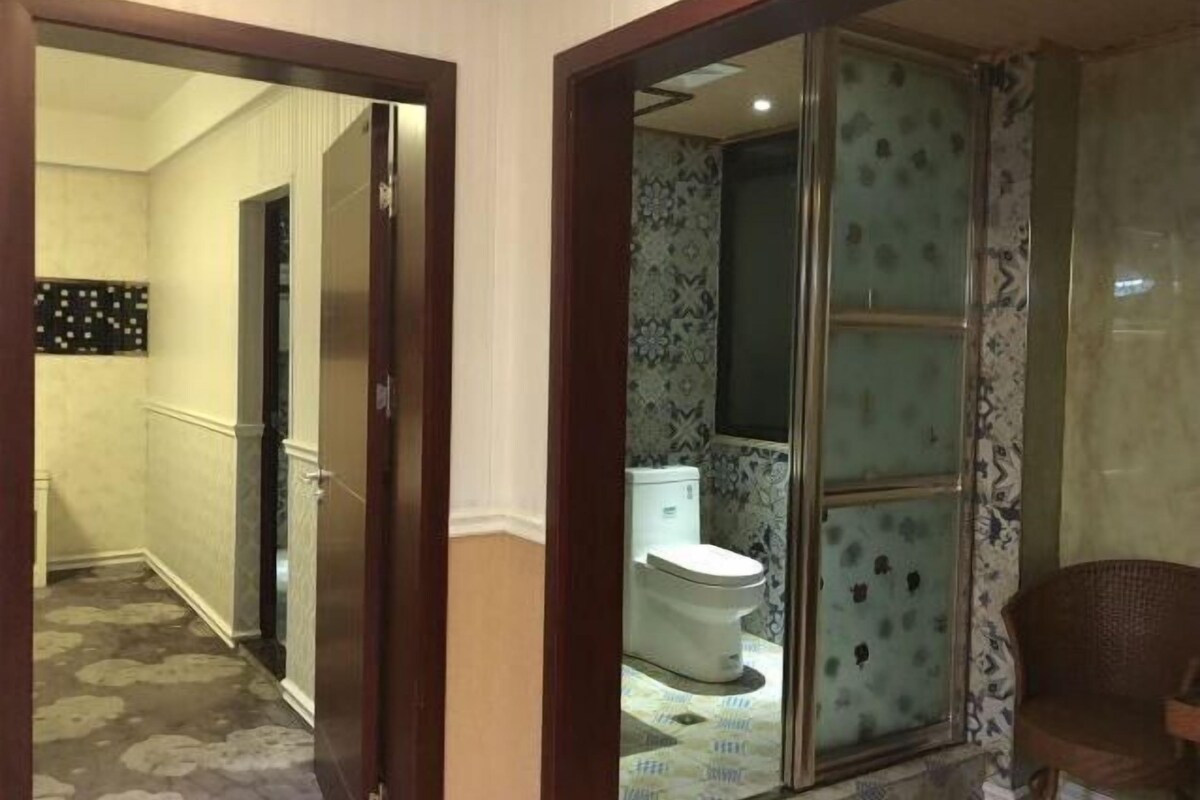 A hotel room with a bathroom featuring a toilet, a shower, and a glass door.