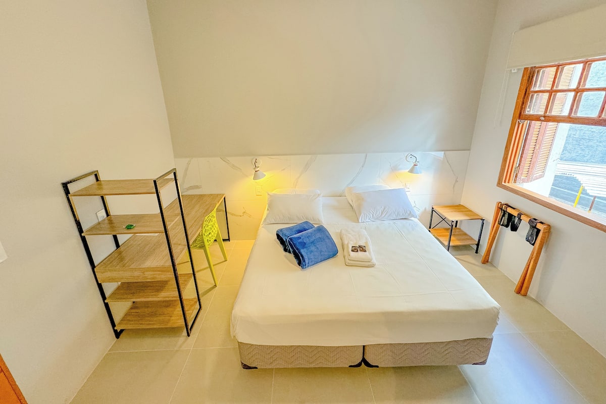 A hotel room with a bed, bedside tables, a window, and a small wooden shelf.