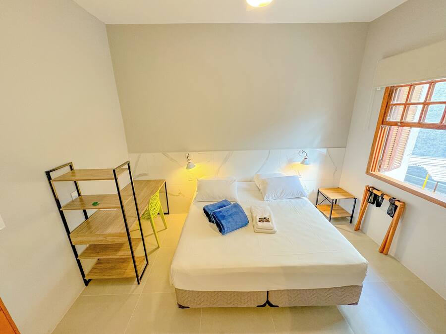 A hotel room with a bed, bedside tables, a window, and a small wooden shelf.