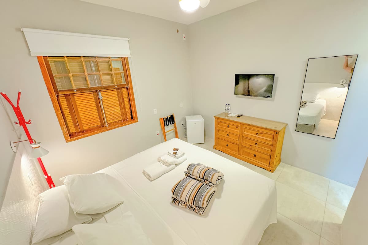 A bedroom with a bed, a wooden dresser, a mirror, a window with blinds, and a ceiling fan.