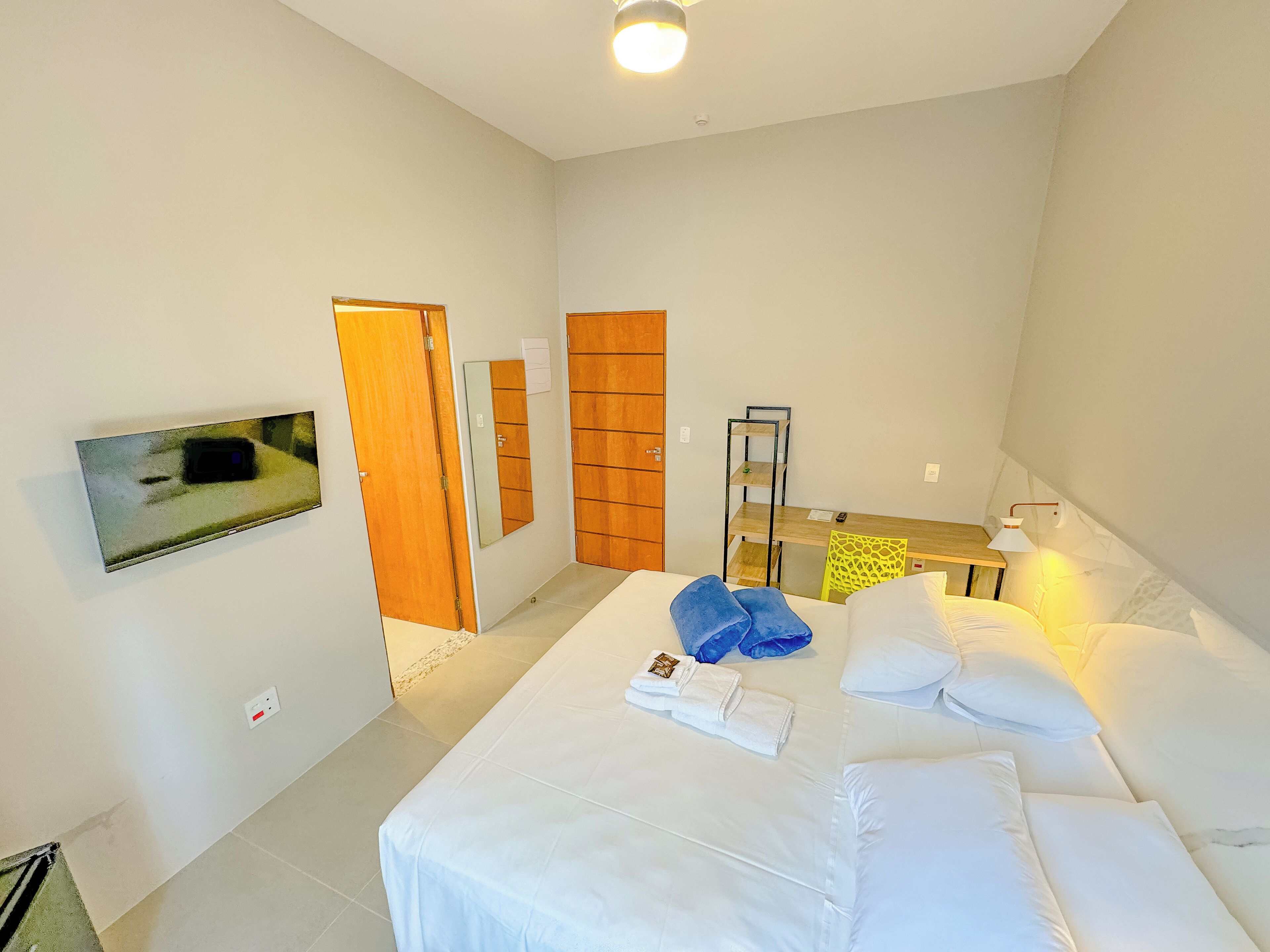 A bedroom with a bed, a desk, a chair, a TV, and a wardrobe.