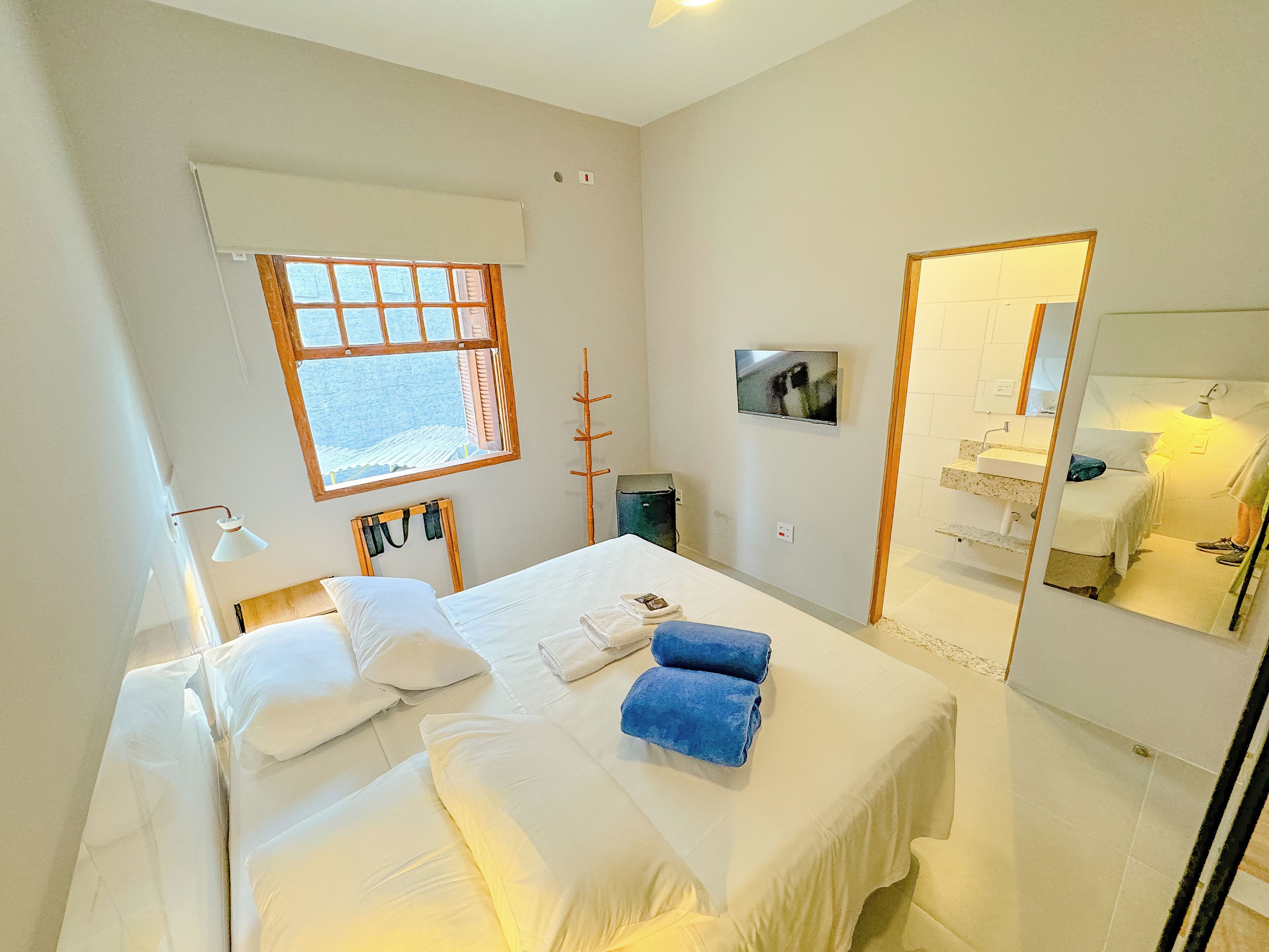 Ett hotellrum med en säng, en stor spegel, en tv och ett fönster med utsikt.