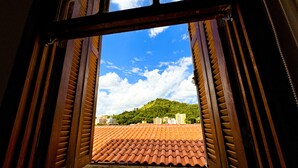 An open wooden door leading to a tiled terrace with a view of a hill and buildings. - Edifício Barros (Serra Negra)