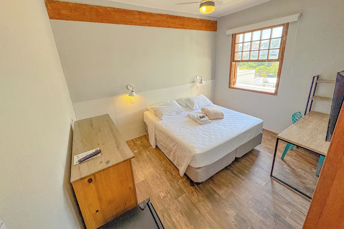 A bedroom with a bed, bedside lamps, a ceiling fan, a window, and a desk with a chair.