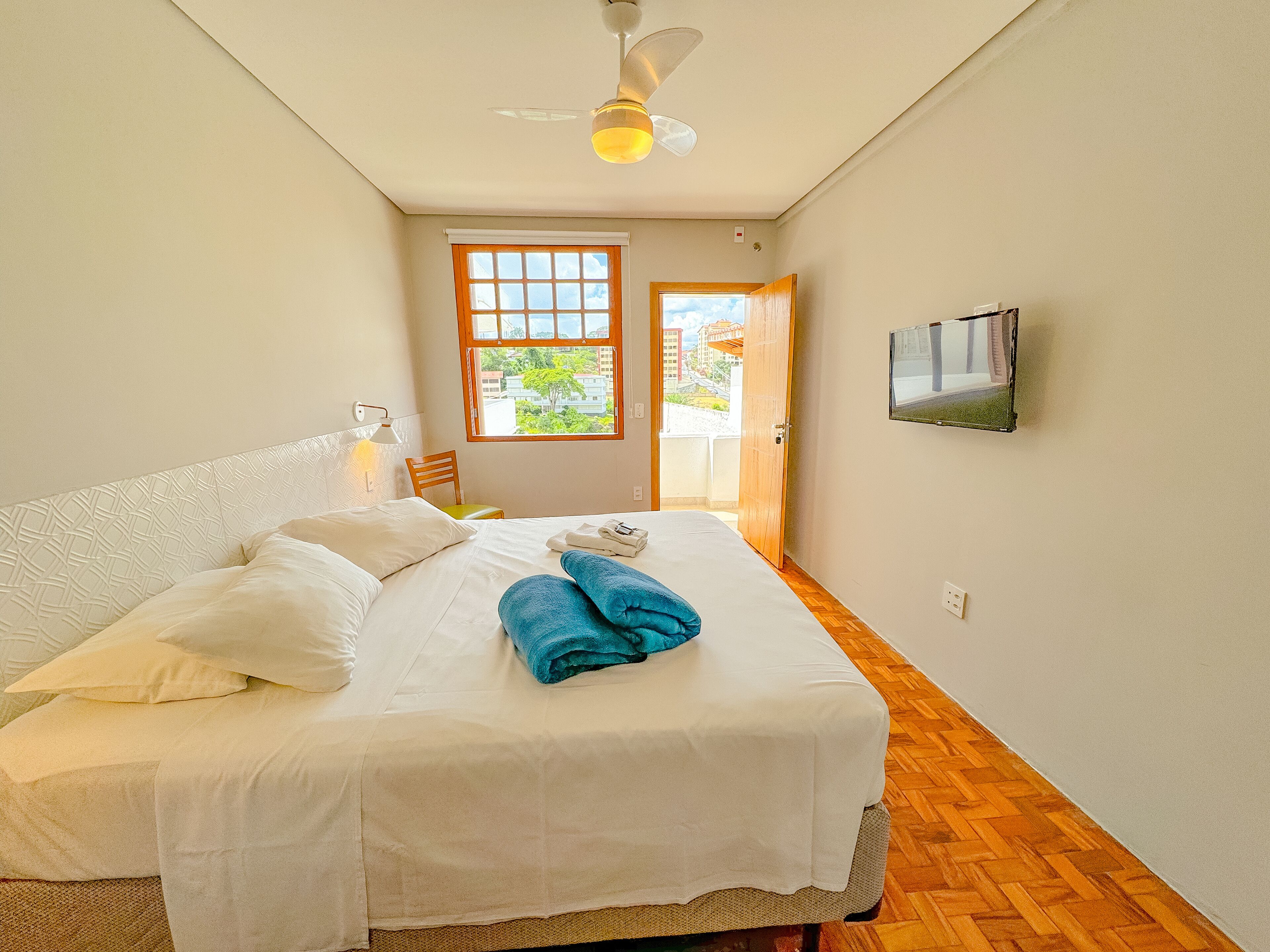A bedroom with a bed, a ceiling fan, a window, and a television on the wall.