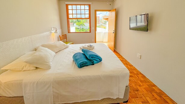 Um quarto com cama, ventoinha no teto, janela e televisão na parede.