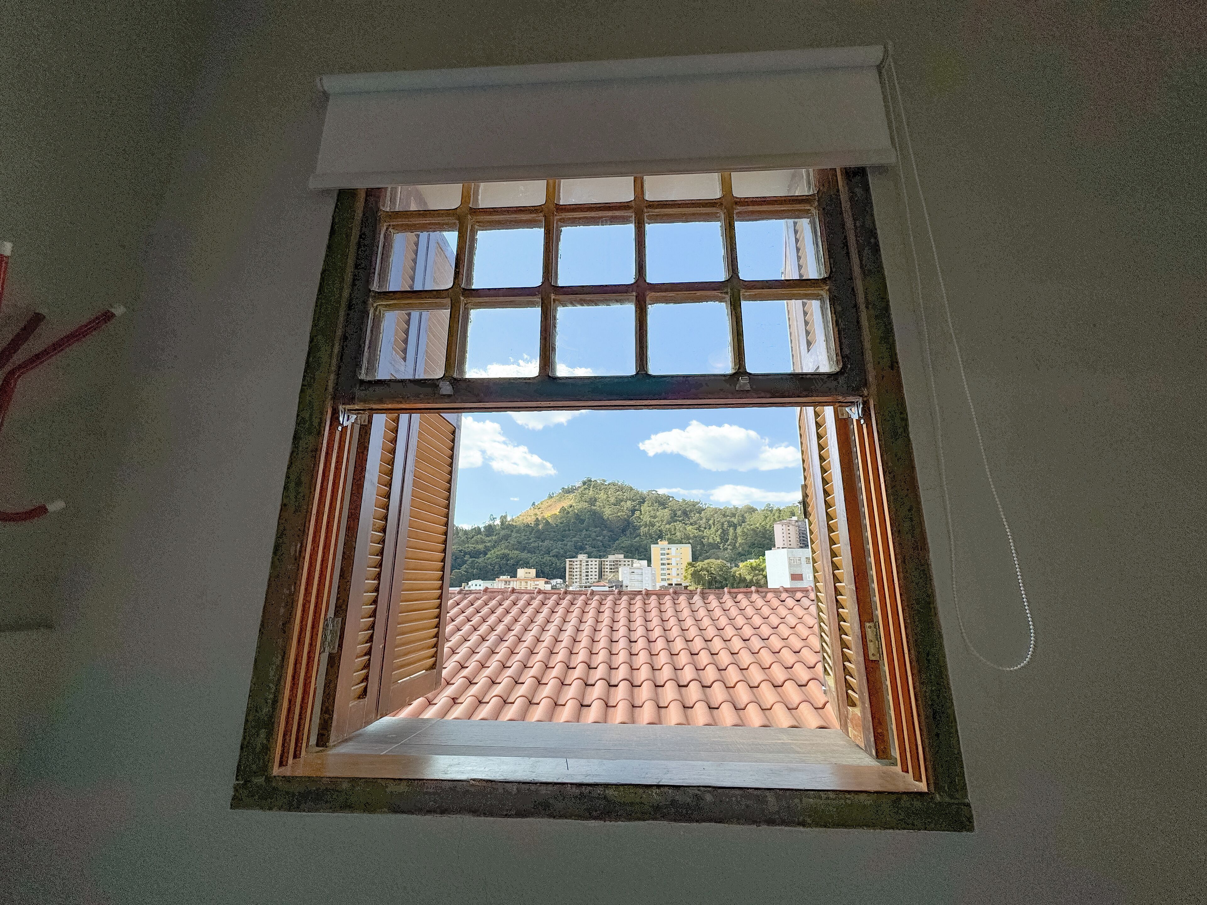 A window with a view of a tiled roof and buildings in the distance.