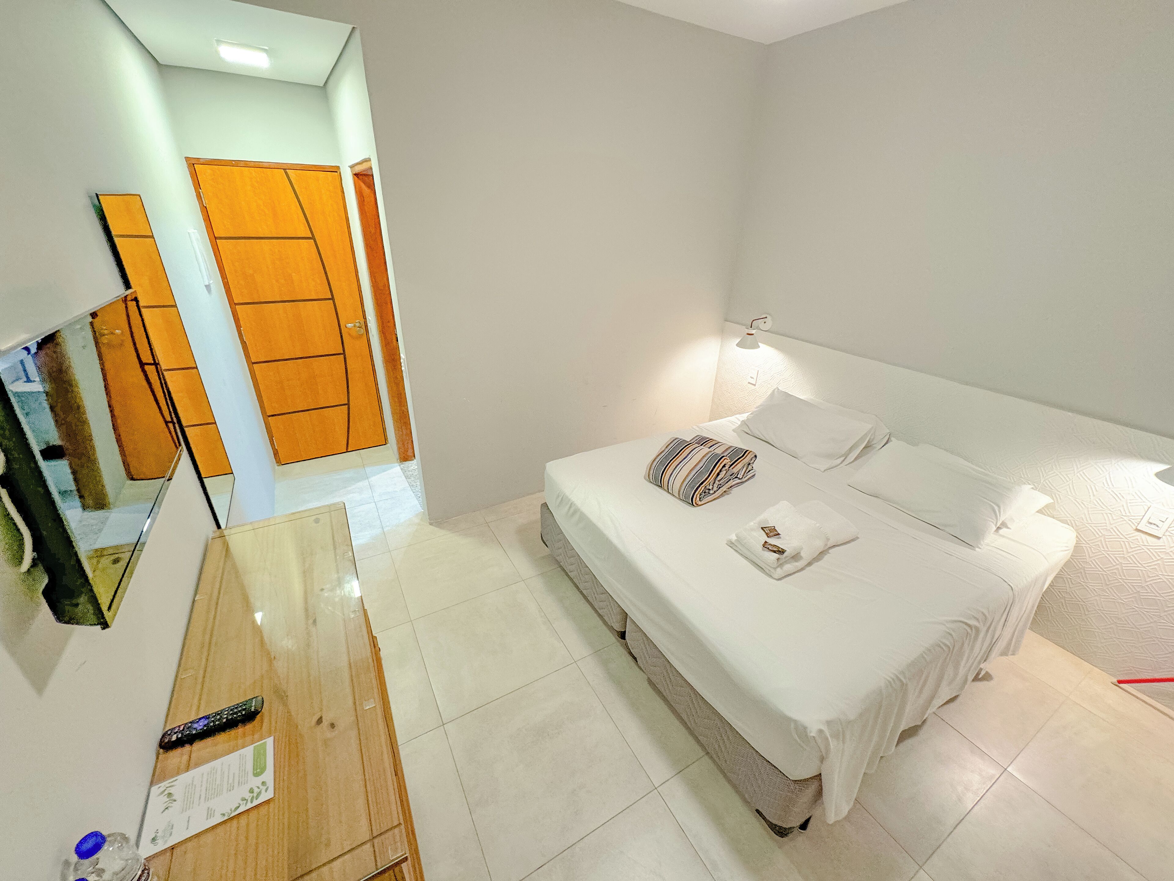 A hotel room with a bed, a bedside table, a mirror, and a wardrobe.
